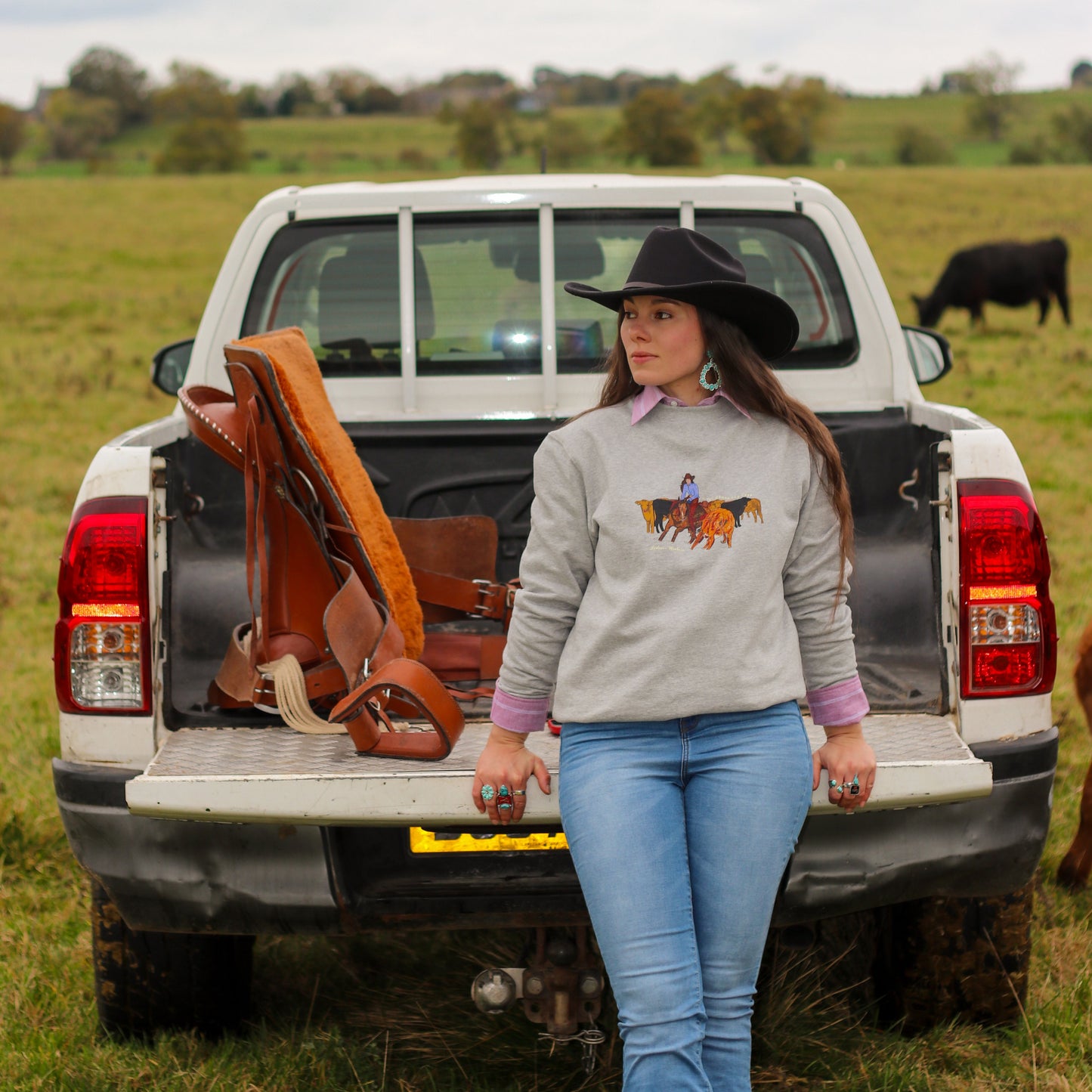 cowgirl on pickup truck, western fashion wearing turquoise jewellery and pearl snap shirt with cattle cutting sweatshirt