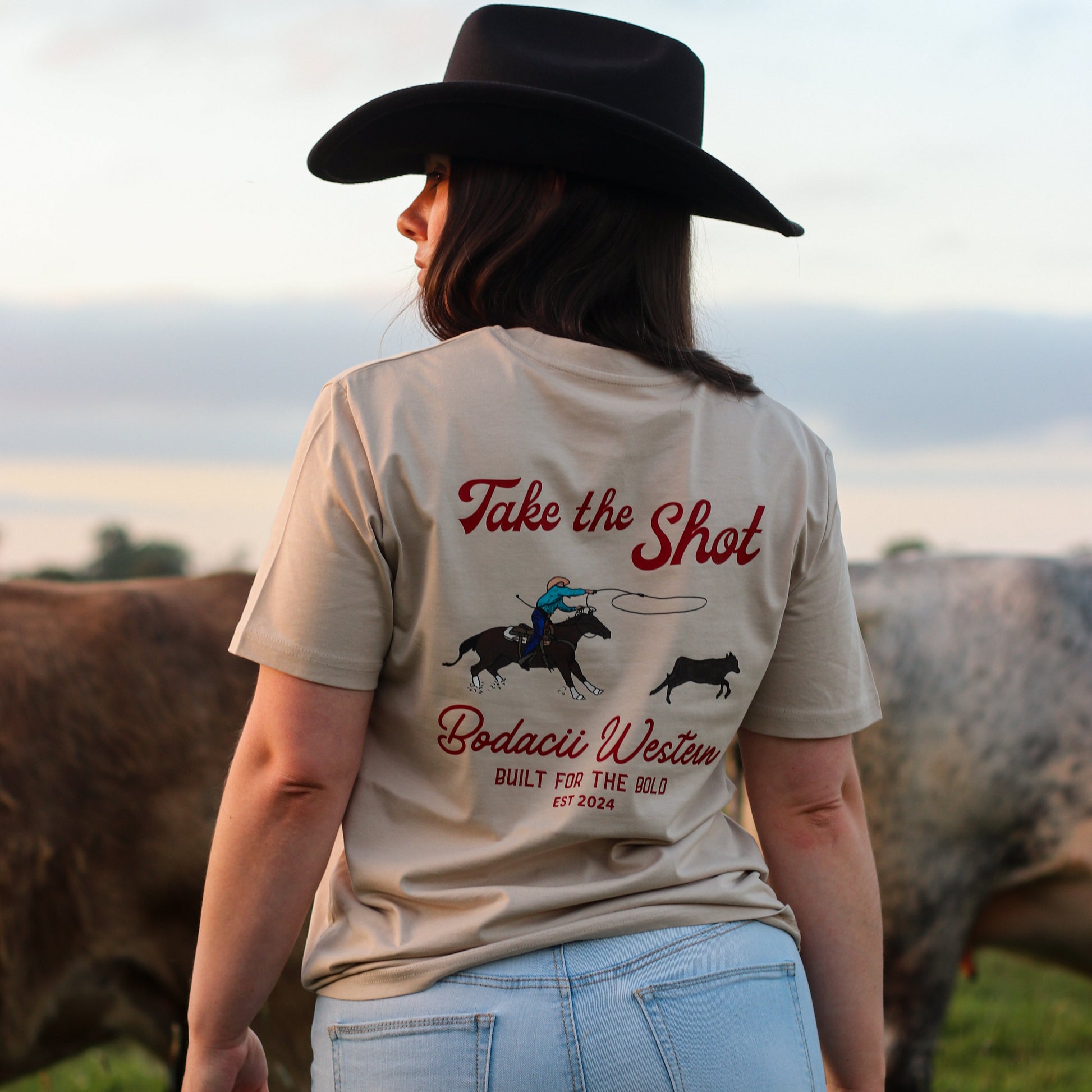 cowgirl wearing roping western tshirt with cattle and sunset