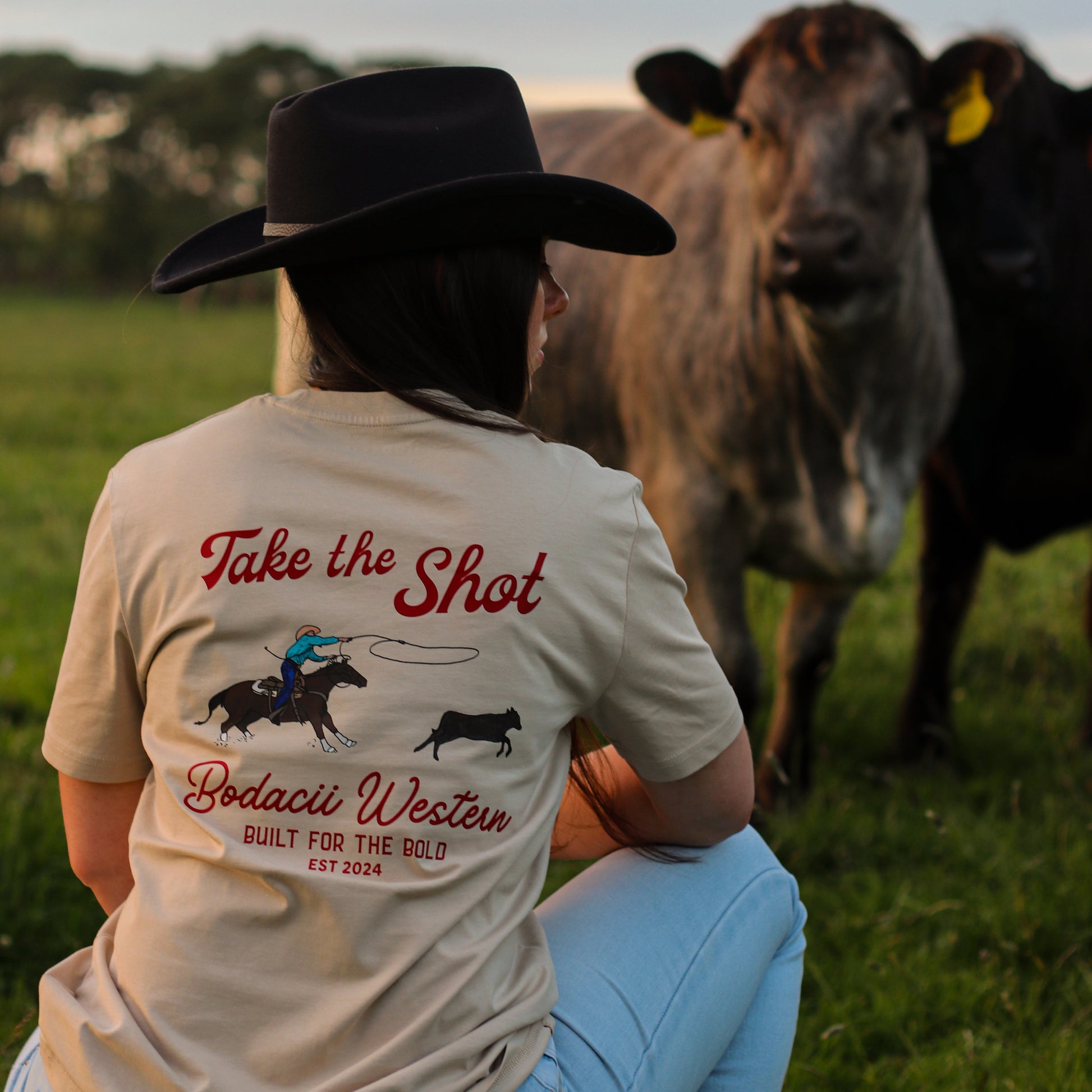 cowgirl wearing roping western tshirt with cattle and sunset