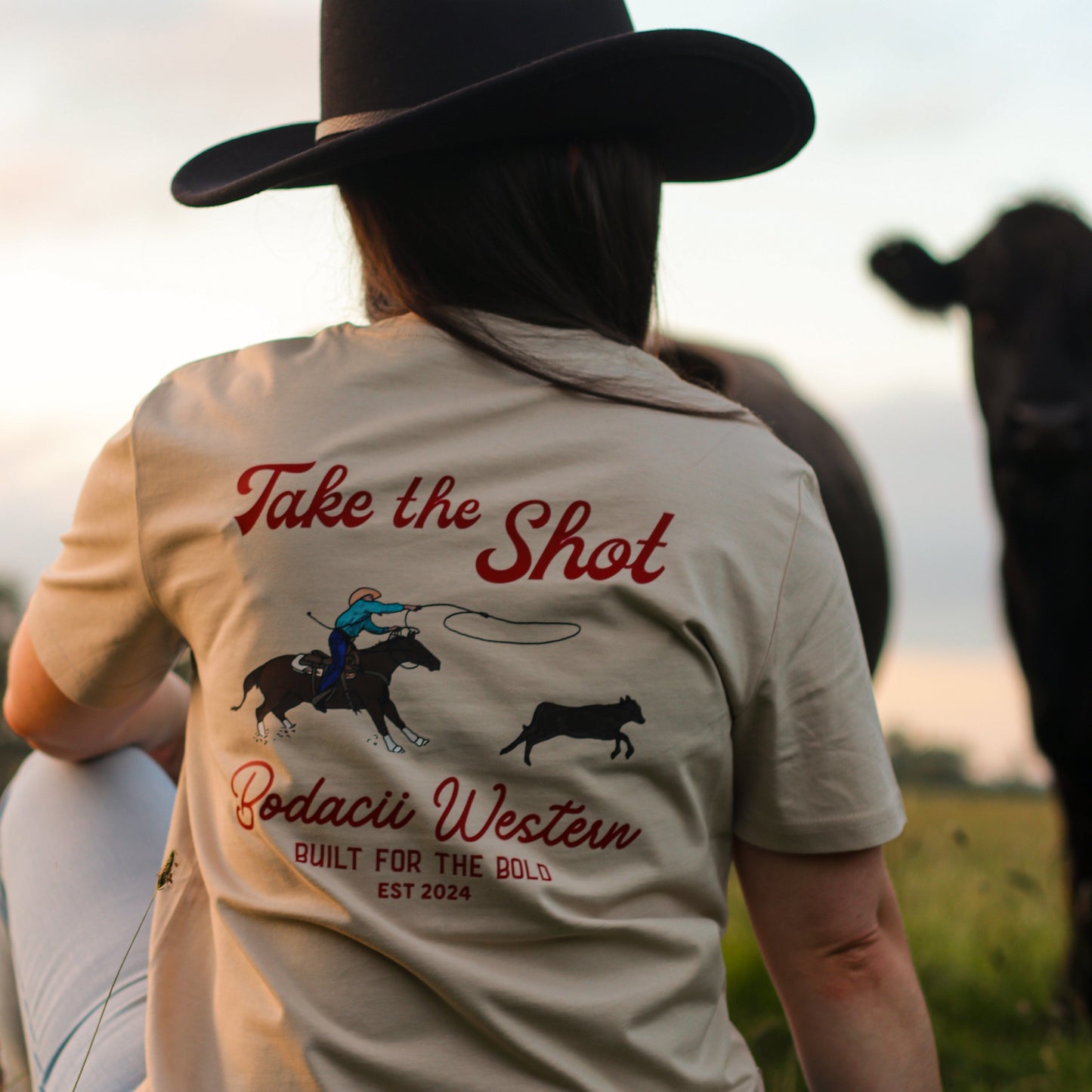 cowgirl wearing roping western tshirt with cattle and sunset
