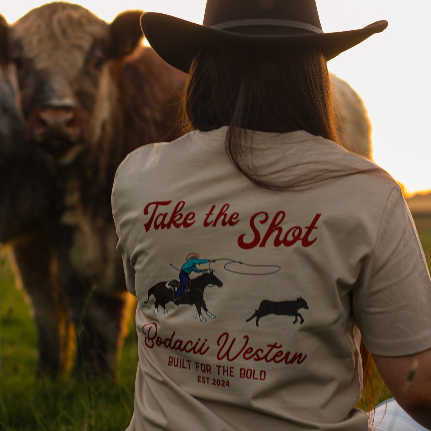 cowgirl wearing roping western tshirt with cattle and sunset