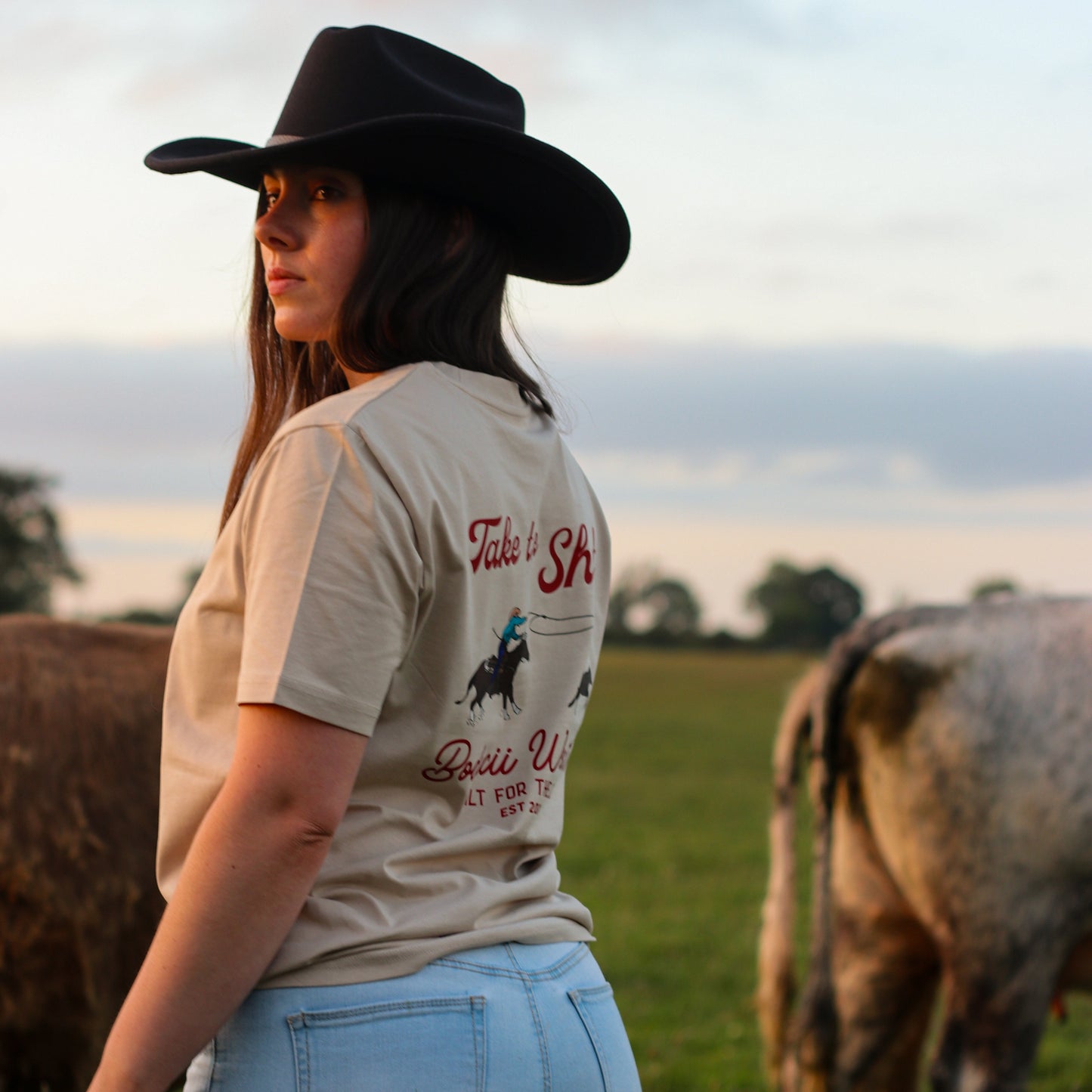 cowgirl wearing roping western tshirt with cattle and sunset