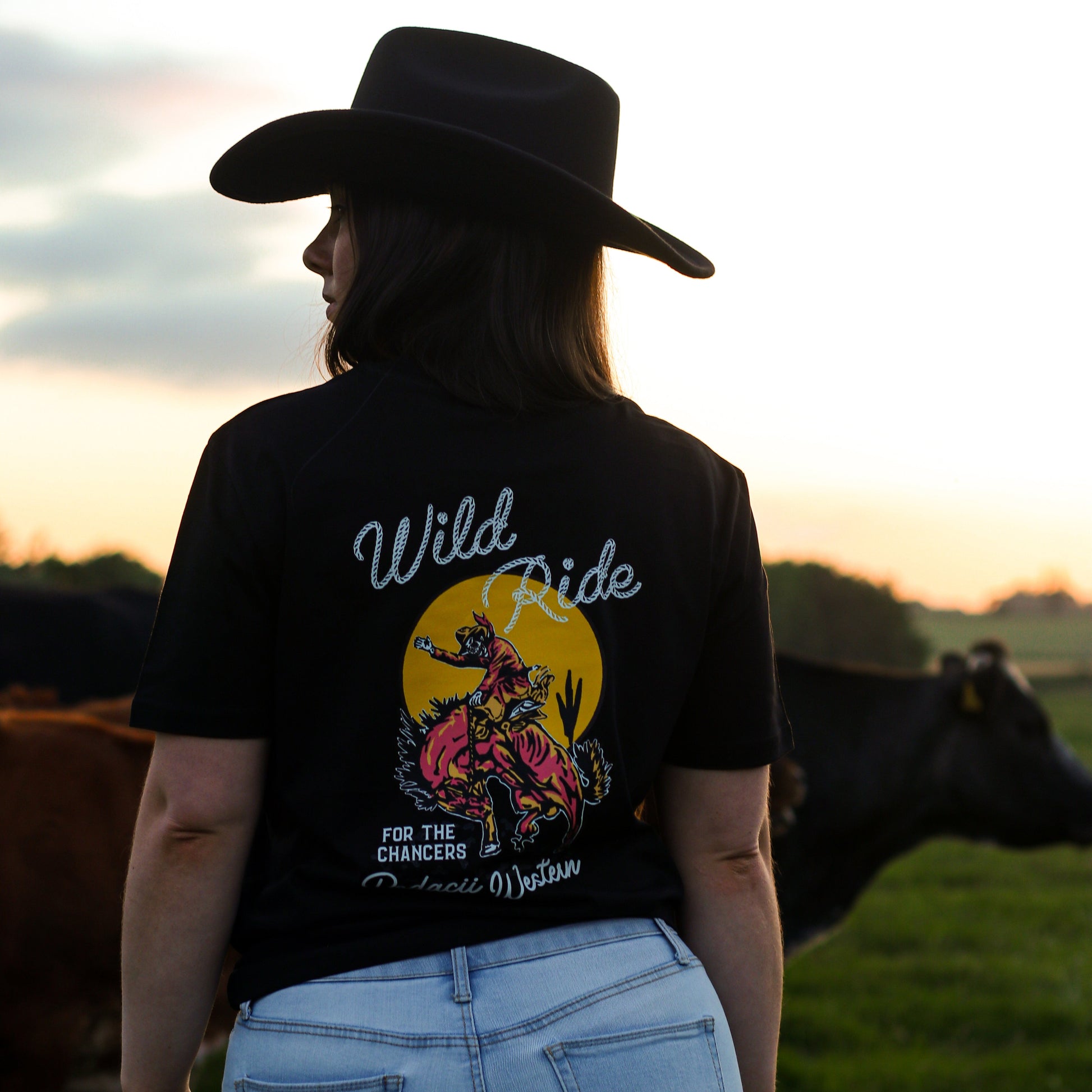 cowgirl wearing western cowboy graphic tshirt in field of cows